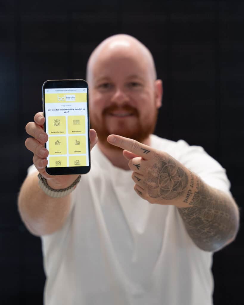Mitarbeiter der bee-doo GmbH zeigt auf ein Smartphone mit geöffneter Anfrageseite für Photovoltaik in Bielefeld